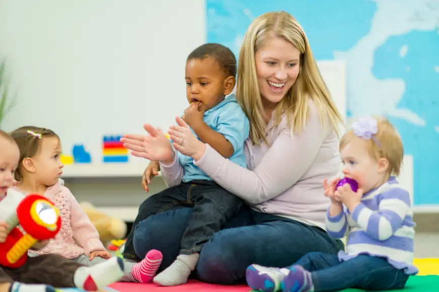 Eine Frau sitzt auf dem Boden mit vier Kleinkindern. Ein Kind sitzt auf ihrem Schoß