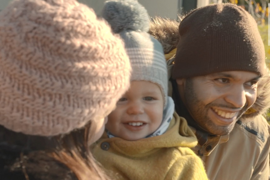 Eine Frau und ein Mann mit Mützen, in ihrer Mitte halten sie ein kleines Kind. Oben rechts das Erfolgsfaktor Familie Logo