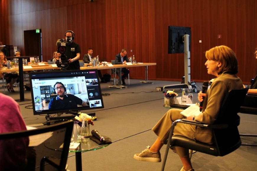 Podiumsdiskussion; Vorne drei Frauen, dahinter zwei Personen mit Kameras und dahinter Menschen die zuhören