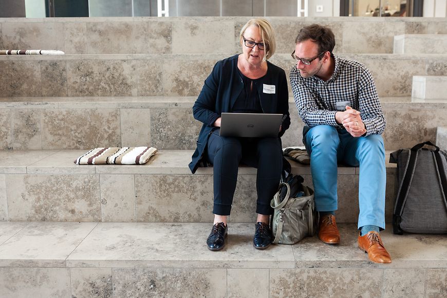 Eine Frau und ein Mann sitzen auf einer Treppe und schauen auf einen Laptop 