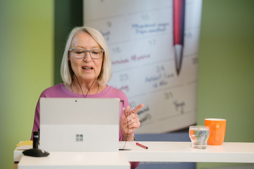 Eine Frau mit Kopfhörern die zu einem Tablet spricht