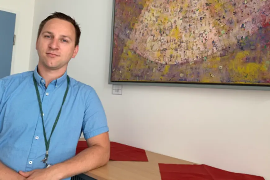 Ein Mann schaut in die Kamera, er lehnt an einem Regal