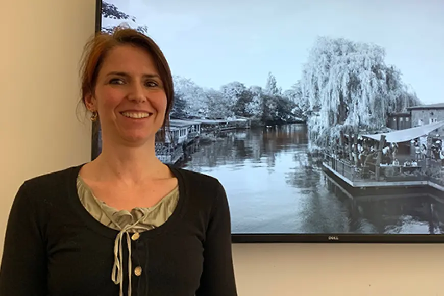 Eine Frau steht vor einem Bildschirm und schaut in die Kamera