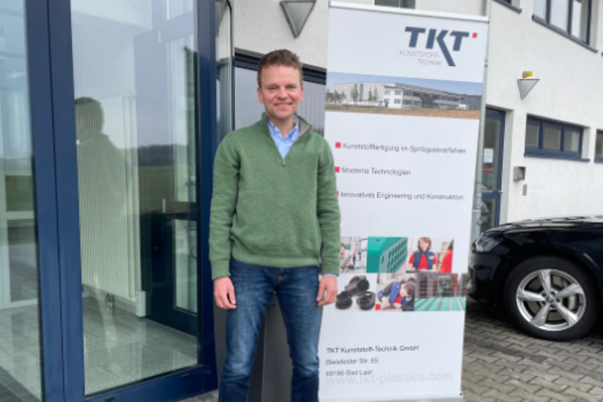 Dr. Peter Brinkmann steht vor einem Gebäude neben einem Aufsteller mit der Aufschrift "TKT"