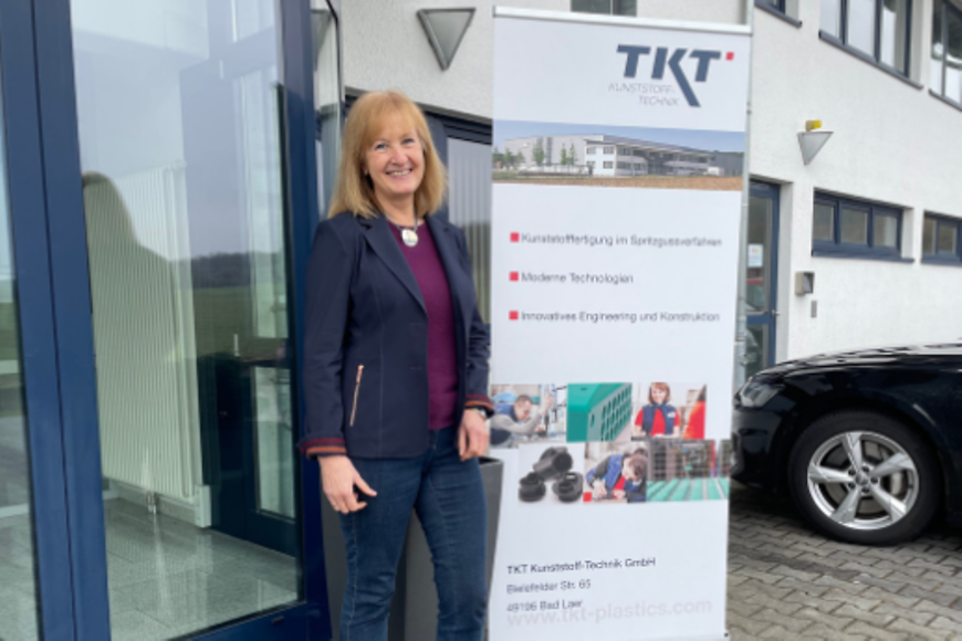 Cornelia Vaupel steht vor einem Gebäude neben einem Aufsteller mit der Aufschrift "TKT"