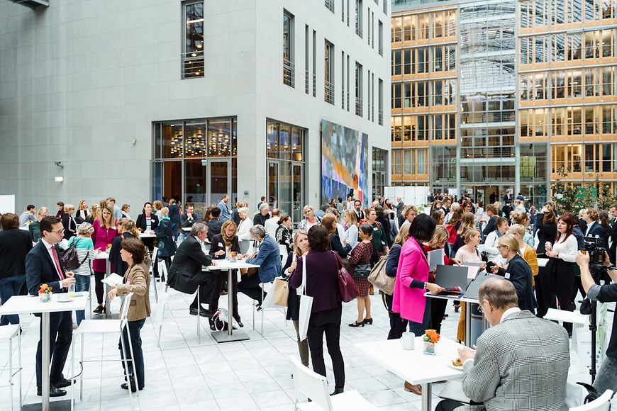 Viele Menschen in einem Atrium an Stehtischen.