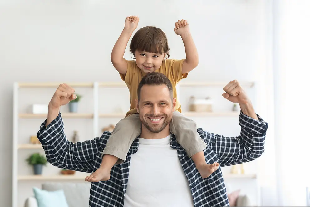 Ein Mann trägt ein Kind auf den Schultern. Beide werfen die Arme in die Luft.