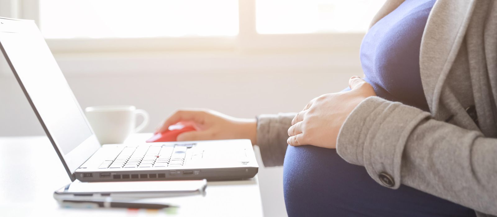Eine schwangere Frau sitzt vor einem Laptop.