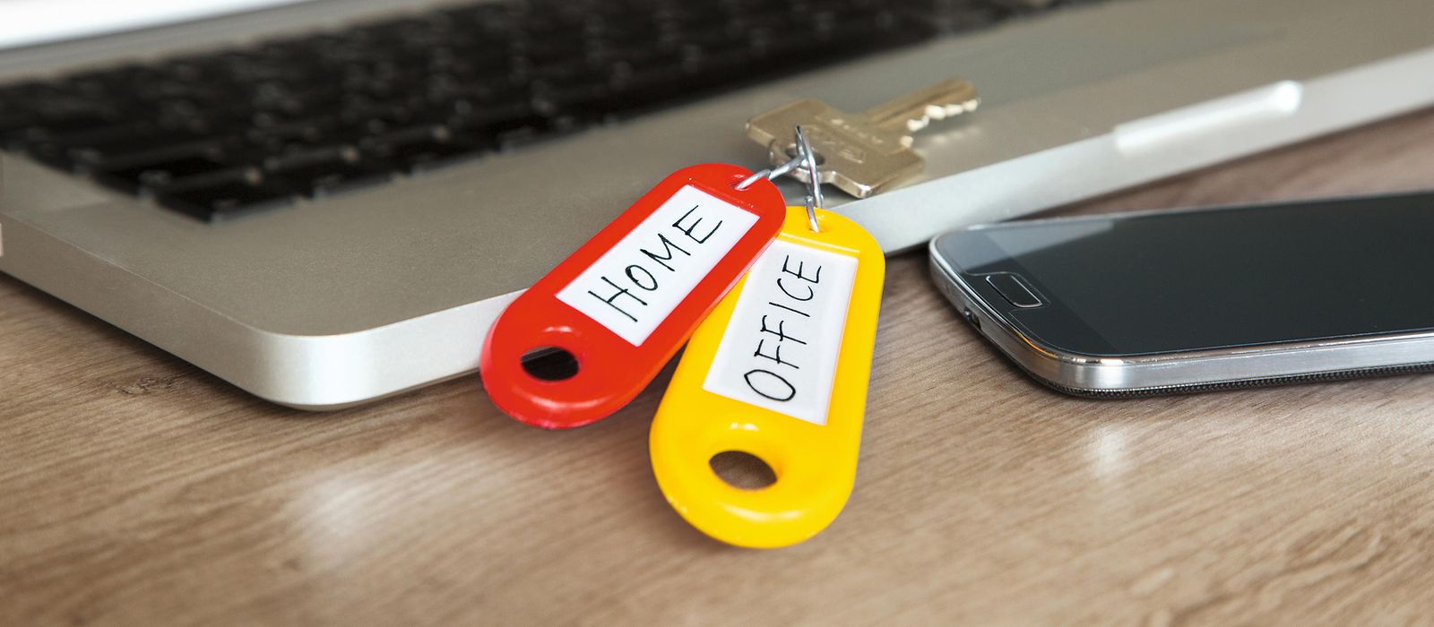 Laptop und Handy sowie ein Schlüssel mit zwei Anhängern. Auf dem einen steht „Home“, „Office“ auf dem anderen Schlüssel 