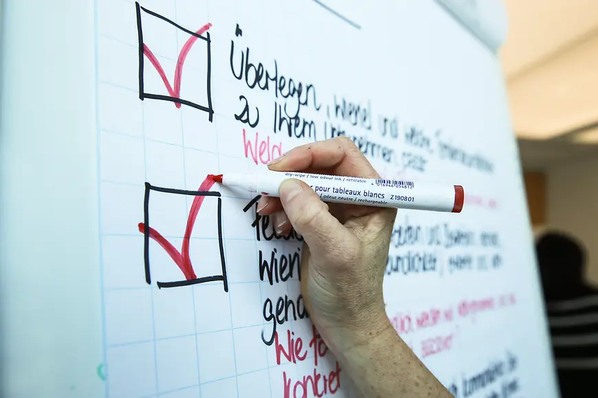 An einer Pinnwand werden Kästchen mit einem roten Stift abgehakt.