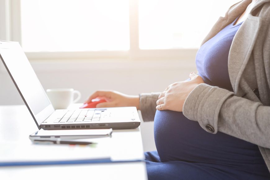 Eine schwangere Frau sitzt an ihrem Laptop
