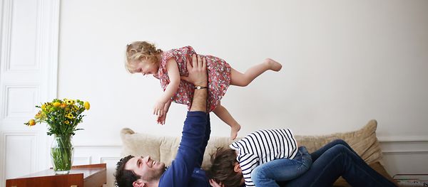 Ein Mann spielt mit zwei Kindern auf einem Sofa