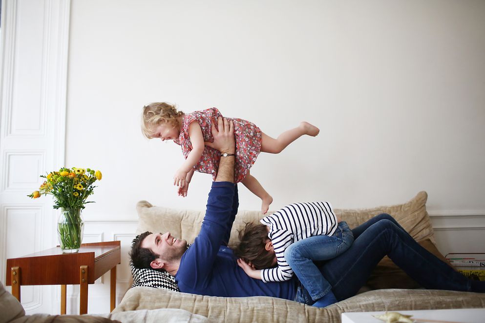 Ein Mann spielt mit zwei Kindern auf einem Sofa