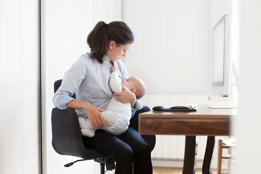 Frau stillt Kind vor dem Computer 