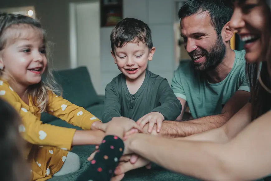 Familie die die Hände in der Mitte übereinander legt. Mutter Vater und zwei Kinder 