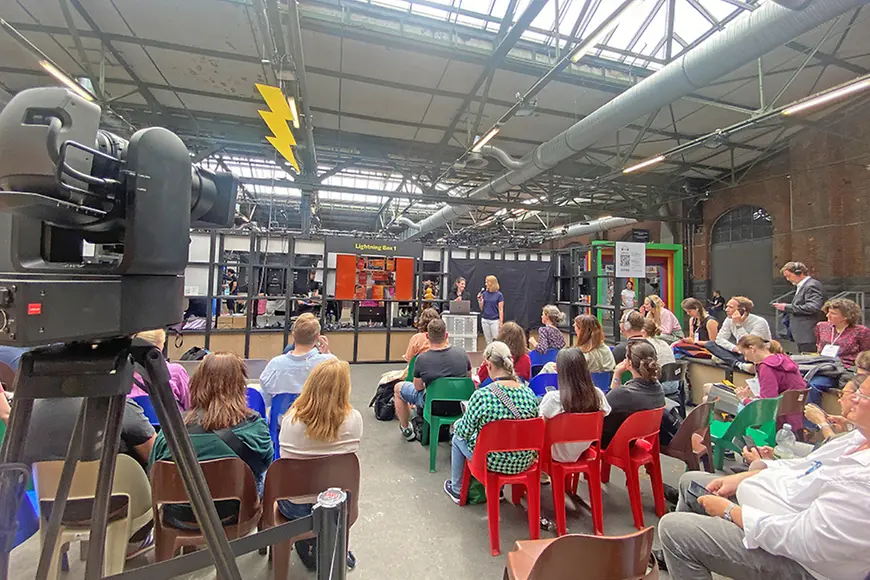 Bild eines Vortrags aus der letzten Reihe geschossen. Zwei Frauen mit Mikrophonen und ein Bildschirm im Hintergrund. 