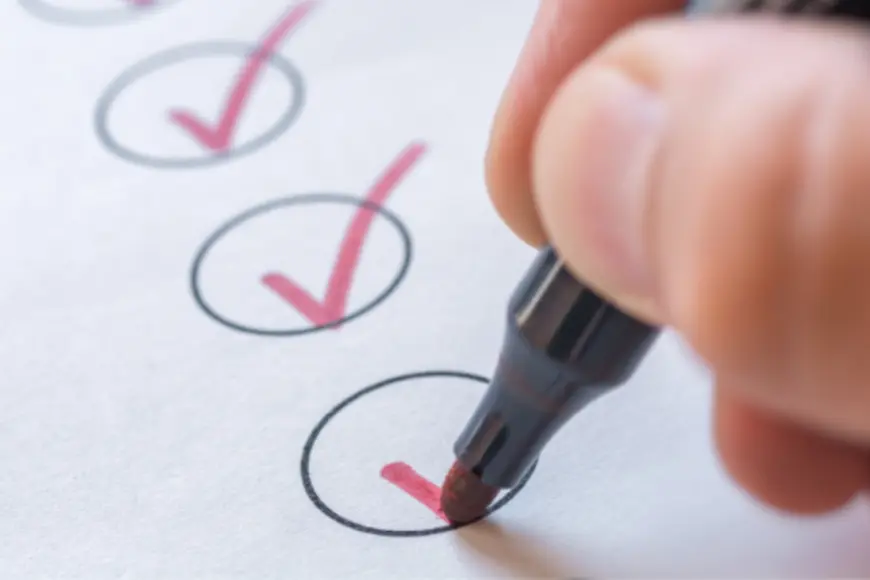 Eine Hand hält eine Stift und kreuzt mit diesem ein Kästchen ab