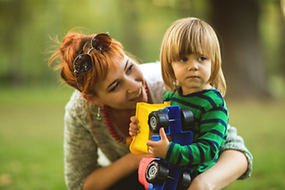 Zu sehen ist eine Mutter im Grünen, die ihr kleines Kind umarmt