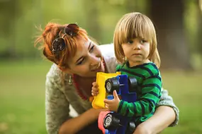 Zu sehen ist eine Mutter im Grünen, die ihr kleines Kind umarmt