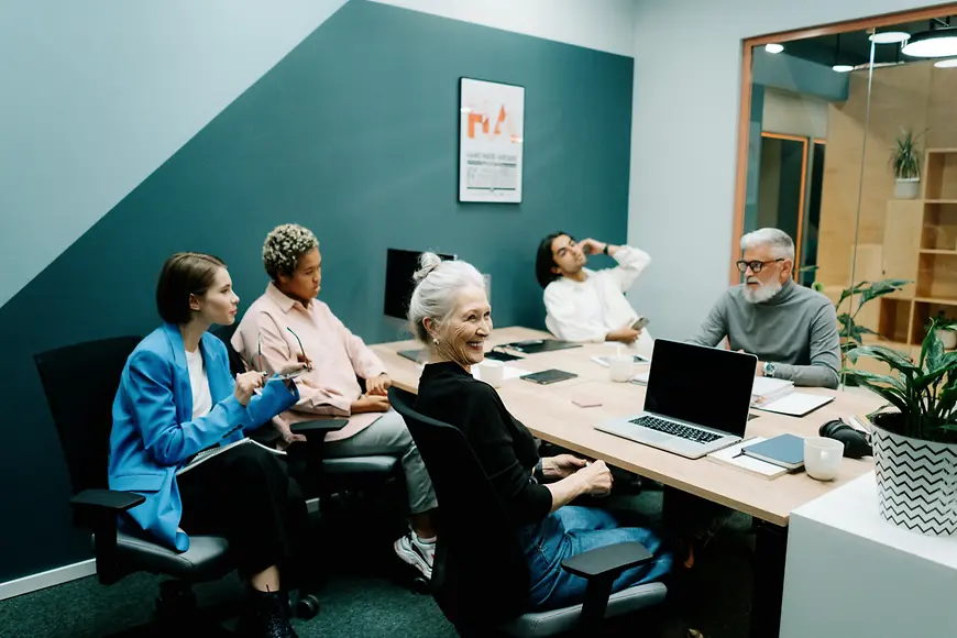 Symbolbild: Ein Team aus Mitarbeitenden unterschiedlichen Alters sitzt gemeinsam an einem Konferenztisch.