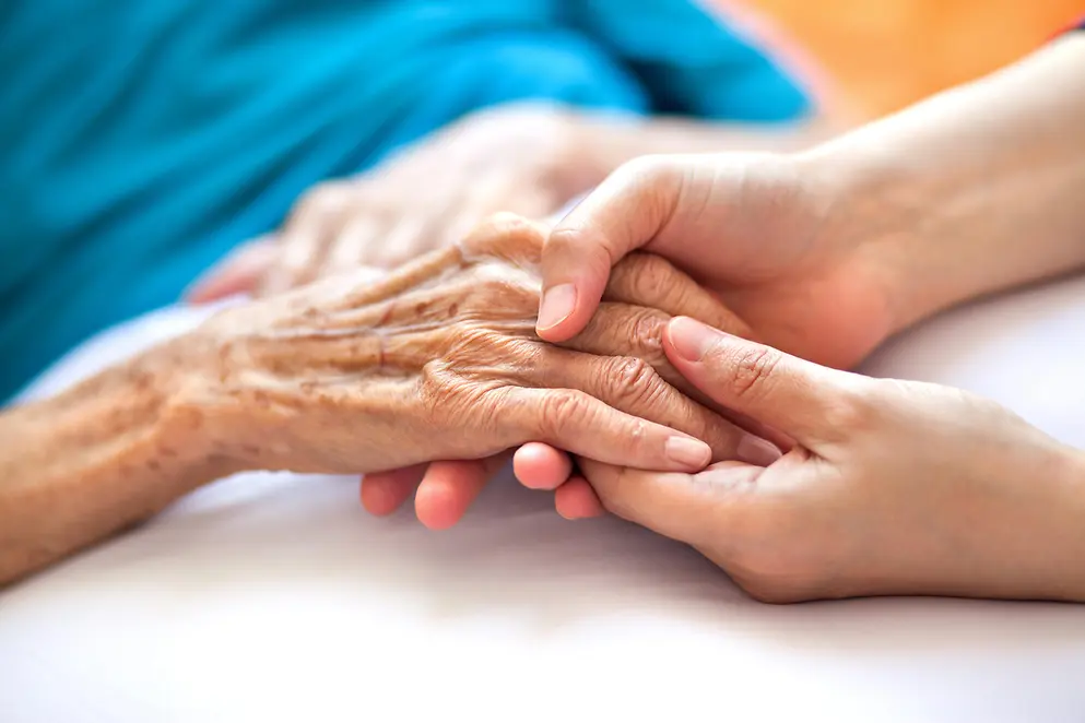 Zusehen sind in einer Nahaufnahme zwei Hände, die die Hand einer älteren Person halten