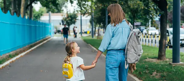 Eine Frau und ein kleines Mädchen spazieren Hände haltend durch einen Park